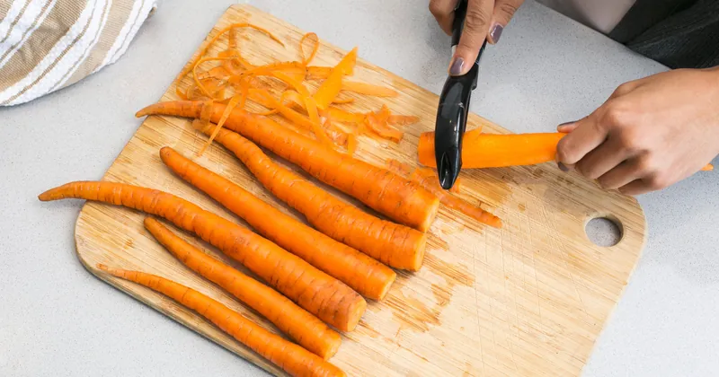 Carrots being peeled on a wooden chopping board