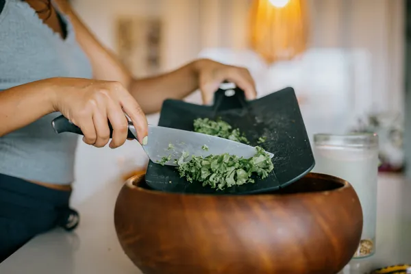Chopped kale being scraped into a wooden salad bowl