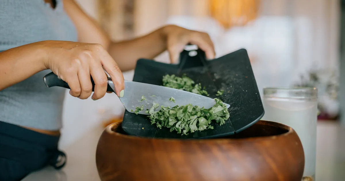 Chopped kale being scraped into a wooden salad bowl
