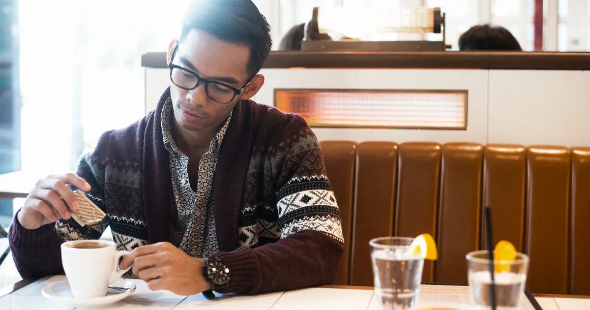 Man adding sugar to his coffee in a cafe